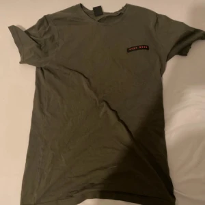 Olivgrön t-shirt från Hugo Boss - Snygg olivgrön t-shirt från Hugo Boss med diskret logotyp på bröstet i svart och rött. Klassisk rund hals och korta ärmar, perfekt för en chill och stilren look. Mjuk bomull som känns skön mot huden. Passar dig som gillar enkel design med.