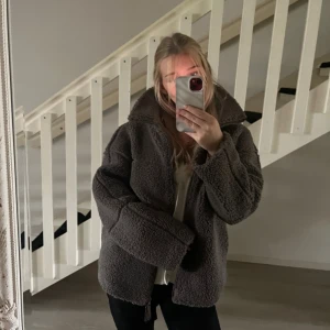 Brun teddyjacka med dragkedja - Mysig brun teddyjacka med hög krage. Jackan har en loose passform och är tillverkad i fluffigt fleece-material. 