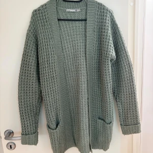 Grön stickad kofta från 157 - Mysig ljusgrön stickad kofta från 157 med grovstickat mönster, två fickor framtill och ribbade muddar. Det är storlek 160 men passar upp till S. Aldrig använd utan endast testad på. 