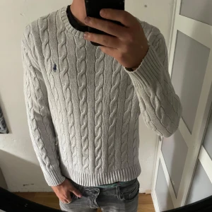 Ljusgrå kabelstickad tröja Polo Ralph Lauren - Säljer en ljusgrå kabelstickad tröja från Polo Ralph Lauren. Klassisk rund halsringning, ribbade muddar och ikoniska broderade loggan på bröstet. Perfekt för dig som gillar stilren och tidlös look. Storlek medium, jätte fint skick. Fraktar snabbt, kom med bud eller frågor!