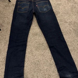 Levi's 512 slim taper mörkblå jeans - Snygga Levi's 512 jeans i mörkblå tvätt med klassiska fem fickor och kontrastsömmar. Modellen har en slim passform och raka ben, perfekt för dig som gillar en modern stil. Tillverkade i slitstarkt jeanstyg med detaljer i kopparfärg.