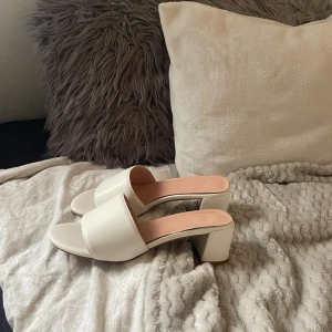 Vita sandaler med blockklack - Stilrena vita sandaler med bred rem över foten och öppen tå. Skorna har en chunky blockklack och platt sula framtill. Insidan är ljusrosa och materialet ser ut som syntet. Perfekta för dig som gillar minimalistisk och modern stil.