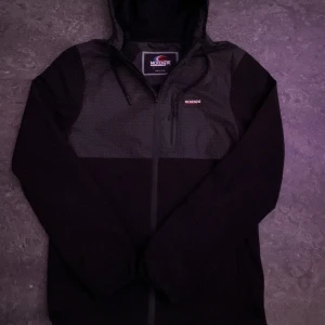 Svart vindjacka från McKenzie med mönster - Säljer en svart vindjacka från McKenzie med huva och dragkedja. Jackan har ett geometriskt mönster i vitt på övre delen och detaljer som snörning vid huvan samt en bröstficka med dragkedja. Perfekt för dig som gillar sportig och stilren look.