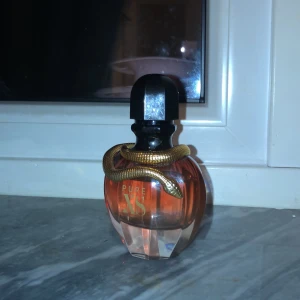 Pure XS Femme Eau de Parfum - En parfym med kryddig doftfamilj och noter av ylang-ylang, vanilj, popcorn, sandelträ och amber. Flaskan har en unik design med en guldfärgad orm, perfekt för dig som vill sticka ut och testa något annorlunda.