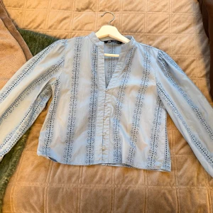 Ljusblå broderad blus från Zara - Supersöt ljusblå blus från Zara med broderade detaljer och knappar framtill i storlek XS. Blusen har lång ärm och ett v-format halslinje. Mönstret består av broderade ränder som ger en chill och feminin vibe. Väldigt bra skick 