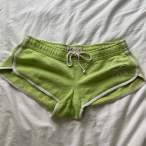 Limegröna shorts från Hollister - Säljer ett par limegröna shorts från Hollister med vit snörning och vita kanter. De har låg midja och är gjorda i mjuk bomullsfrotté. Perfekta för chill dagar eller träning. Hollister-logga broderad framtill.