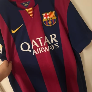 FC Barcelona matchtröja 2014 - Säljer en officiell FC Barcelona matchtröja 2014 från Nike, (ÄKTA). Tröjan har breda marinblå och vinröda ränder och broderade klubb- och LFP-emblem. Materialet är Dri-Fit polyester, perfekt för fotboll. Sponsorer: Qatar Airways och UNICEF. Knappt använd pga för stor. Hör av er vid funderingar!!