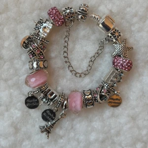 Charmarmband med rosa och silver detaljer - Unikt charmarmband med flera berlocker i silverfärg och rosa toner, bland annat stjärna, Eiffeltorn, hjärtan och texten 'Happy Birthday'. Vissa berlocker är glittriga och har pärlor. Perfekt för dig som gillar personliga smycken med mycket detaljer.