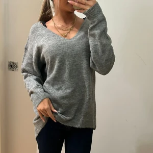 Grå stickad v-ringad tröja - Mysig grå stickad tröja med v-ringad hals och långa ärmar. Modellen är loose fit och har ribbade muddar vid ärmslut och nederkant. Perfekt för dig som gillar en chill och avslappnad stil. Passar till jeans eller leggings för en enkel look.