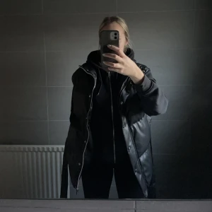 Tjockare väst  - En perfekt väst till hösten/våren, svart längre tjockare väst med dragkedja, knappar och band + fickor på sidan. Använd fåtal gånger, väldigt fint skick 