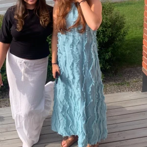 Ljusblå långklänning från Zara - Säljer en ljusblå långklänning från Zara med coola fransdetaljer i vågiga rader över hela klänningen. Klänningen har smala axelband och är ärmlös, vilket ger en chill och somrig vibe. Materialet är lätt och känns luftigt, perfekt för varma dagar.