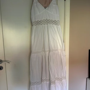 Vit långklänning med spets från Zara - Superfin vit långklänning från Zara med tunna axelband och v-ringad hals. Klänningen har flera spetsdetaljer och smock vid bysten för extra komfort. Tillverkad i mjuk bomull, perfekt för varma dagar. Flowy och romantisk stil med boho-vibe.