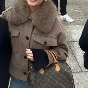 Meotine kappa  - Snygg brun pälskappa från Meotine med stor fluffig krage i päls. Jackan har två stora fickor med lock och knappar framtill. Knapparna på fickorna fram har tyvärr lossnat och tappats bort men går att sätta dit med vanliga svarta knappar. XS/S är storleken.