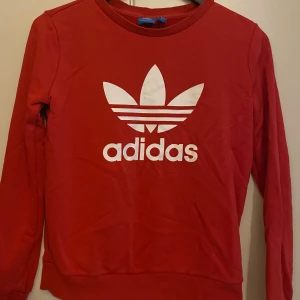 Röd Adidas tröja med logga - Röd långärmad tröja från Adidas med stor vit logga. Den har ribbade muddar vid ärmslut och nederkant. Skulle säga strl Xs och S