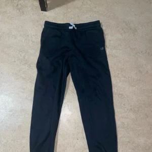 Svarta mjukisbyxor från CZ Original - Svarta mjukisbyxor från CZ Original med dragsko i midjan och två fickor framtill. Byxorna har en enkel och stilren design med en liten logga på ena fickan. Perfekta för chill dagar eller när du vill ha det extra bekvämt.