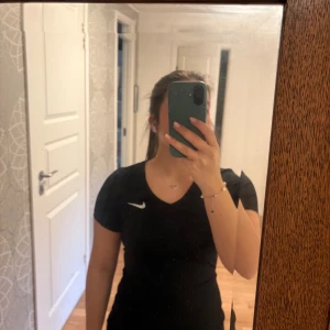 Svart Nike träningstopp - Säljer en svart träningstopp från Nike med v-ringad hals och korta ärmar. Toppen har en slim passform och är tillverkad i ett mjukt och stretchigt material som passar perfekt för gymmet eller löpning. Sparsamt använd så fint skick. Djur och rökfritt hem. 