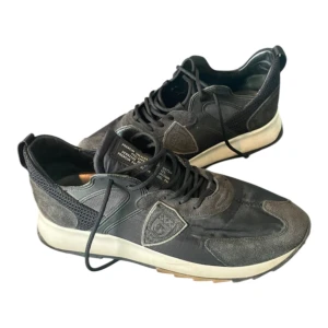 Svarta sneakers från Philippe Model - Svarta sneakers från Philippe Model med snygga detaljer i mocka och mesh. Skorna har snörning, rund tå och en vit sula . Märkets logga syns på sidan och designen är sportig men stilren.