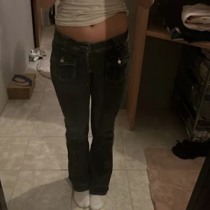 Svarta bootcut jeans Gina Tricot 164  - Svarta jeans från Gina Tricot i storlek 164 med bootcut-modell. Snygga fickor med lock och knappar både fram och bak, samt markerade sömmar. Jeansen har låg midja och är tillverkade i klassiskt denimtyg.