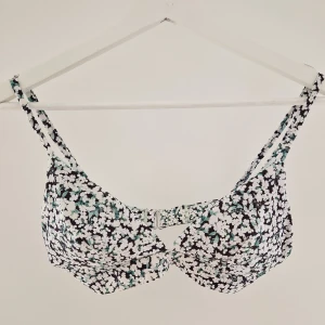 Blommig bikiniöverdel från H&M - Supersöt bikiniöverdel från H&M med blommigt mönster i vitt, svart och grönt. Justerbara axelband och snygg knäppning bak. Utsidan är i stretchig polyester/elastan och insidan är ljusgrön. Perfekt för strandhäng i sommar!