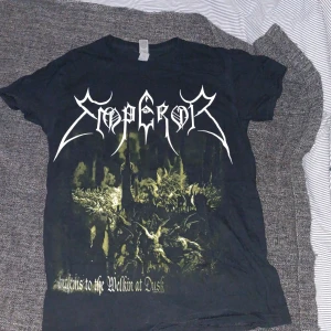 Emperor band t-shirt svart - Svart t-shirt med Emperor-logga och albumomslag från 'Anthems to the Welkin at Dusk' på framsidan. Baksidan har fyra sepiafärgade bandporträtt. Klassisk passform och tryck i vitt och gulgrönt. Perfekt för metalheads som vill visa sin stil.