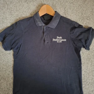 Mörkblå pikétröja från Peak Performance - Snygg mörkblå pikétröja från Peak Performance. Nypris 500 kr.                                                            Klassisk krage och två knappar framtill. Broderad logga på bröstet. Perfekt för en sportig och stilren look. Skön bomullskvalitet och korta ärmar.