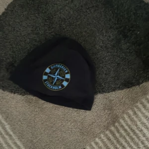 Svart Djurgården mössa Djurgården Stockholm utan offer ingen seger  - Svart mössa med Djurgården Stockholm-logga framtill i blått, vitt och guld. Klassisk passform och mjukt material som passar perfekt för kyliga dagar. Snygg accessoar för alla Djurgården-fans.