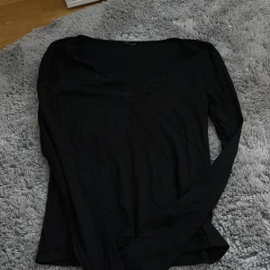 Svart långärmad blus med spets från lager 157 - Svart långärmad blus med v-ringning och diskret spetsdetalj runt halsen. Tunn och mjuk i materialet, perfekt att styla med jeans eller kjol. Enkel och stilren design som funkar till många looks.
