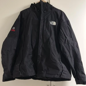 Svart vindjacka The North Face XL - Svart vindjacka från The North Face Summit Series i storlek XL. Jackan har huva, dragkedja, flera fickor och broderad logga på bröstet. Materialet är slitstark nylon med Gore-Tex, perfekt för blåsiga och regniga dagar. Använt mycket, den är lite sliten därav priset (Säljer dock väldigt billigt) Lite sliten på ena armen, men inget man tänker på.