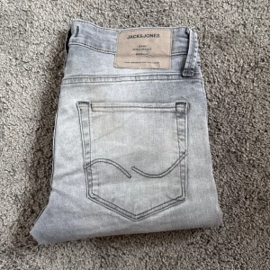 Grå jeans från Jack & Jones - Snygga grå jeans från Jack & Jones med klassisk fyrficksdesign. Jeansen har en normal passform och är tillverkade i mjukt jeanstyg med knapp och dragkedja framtill. Perfekt för dig som gillar en avslappnad stil.