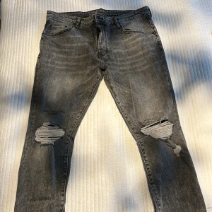 Grå ripped jeans från Dsquared2 - Snygga grå jeans från Dsquared2 med slitna detaljer och textbroderi vid knäna. Modellen har en slim passform och klassisk femficksdesign. Jeansen är tillverkade i denim och har en cool, tvättad look med råa hål på båda benen.