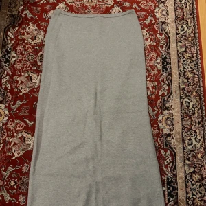 Grå långkjol från Gina Tricot - Säljer en stilren grå långkjol från Gina Tricot. Kjolen är rak i modellen och har en mjuk, stickad känsla som gör den superbekväm. Perfekt att matcha med en enkel topp eller kofta för en clean look. Den är en set, har tröjan.