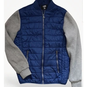 Blå quiltad jacka FSBN XS  - Snygg quiltad jacka från FSBN i marinblått med grå ärmar. Jackan har dragkedja framtill, två fickor med dragkedja och ribbade muddar. Perfekt för dig som gillar en sportig och casual stil. Materialet är polyester och bomull för skön komfort.. 