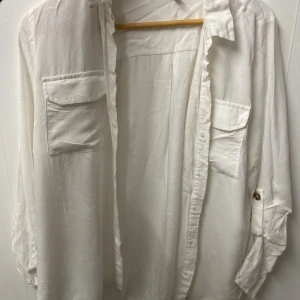 Vit oversized skjorta med fickor - Stilren vit skjorta i oversized modell med två stora bröstfickor och knappar framtill. Skjortan har långa ärmar med knappdetalj så de kan rullas upp. 