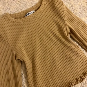 Beige ribbad tröja - Säljer en beige ribbad tröja från FB Sister i storlek XS. Tröjan har långa ärmar, rund halsringning och en söt volangkant nertill. Perfekt för dig som gillar en enkel men trendig stil.