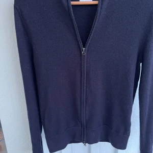 Mörkblå kofta med dragkedja - En stilren Mörkblå kofta med hel dragkedja framtill och långärmad design. Tröjan har en enkel, klassisk look med ribbad krage och muddar. Perfekt för dig som gillar minimalistiska plagg och vill ha något som funkar till många olika outfits.