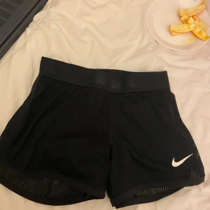 Svarta Nike Dri-Fit träningsshorts XS - Säljer ett par svarta Nike Dri-Fit shorts i meshmaterial med elastisk midja och vit swoosh-logga framtill. Perfekta för träning eller löpning, lätta och andas bra. Klassisk sportig look med diskret 'Just Do It'-text i midjan.