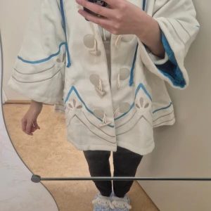 Vit och blå oversize Venti Cloak  - Venti cloak från Ventis Vision med blå detaljer och mönster, vida ärmar och blått mjukt foder. Jackan har snörning framtill, stora dekorativa knappar och en stor huva. Helt ny, oanvänd, endast provad.