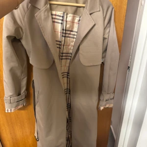 Beige trenchcoat med rutigt foder - Snygg beige trenchcoat från Burberry med klassiskt rutigt foder i beige. 