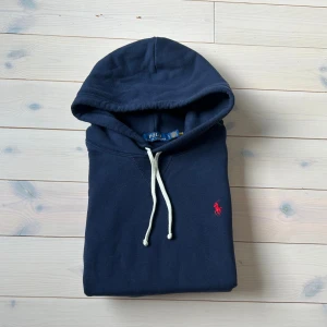 Ralph Lauren hoodie - Snygg marinblå hoodie från Polo Ralph Lauren med klassisk röd broderad logga på bröstet. Använt ett fåtal gånger och tvättad två gånger, väldigt bra skick, inga defekter, originellt köpt på boozt, äkta med qr kod, storlek large men sitter som en stor M eller en liten L, pris går att diskutera vid snabb affär✅