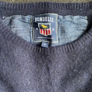 Mörkblå stickad tröja från Bondelid - Mysig mörkblå stickad tröja från Bondelid med rund halsringning och ribbade muddar. Perfekt för kyliga dagar och enkel att matcha med jeans eller kjol. Klassisk och stilren design som funkar året om.
