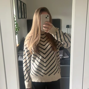 Randig stickad tröja från MNG str S - Säljer en mysig stickad tröja från MNG i beige med svarta ränder i ett snyggt V-mönster. Tröjan har lång ärm, ribbad hög hals och är loose fit. Perfekt för dig som gillar chill och stilren look. Fråga gärna om fler bilder eller info!