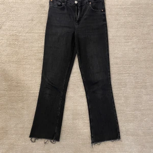 Grå bootcut jeans med rå kant - Grå jeans med bootcut passform och rå, fransad kant vid bensluten. Klassisk femficksmodell med knapp och dragkedja framtill. Snygg mörk tvätt.