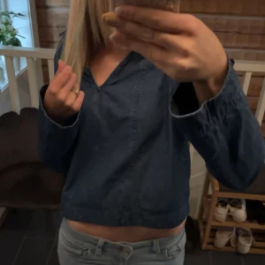 Blå croppad långärmad tröja - Säljer en blå croppad tröja med v-ringad hals och långa ärmar. Tröjan har en avslappnad passform och är gjord i ett denimliknande bomullsmaterial. Perfekt för dig som gillar en chill och enkel stil.