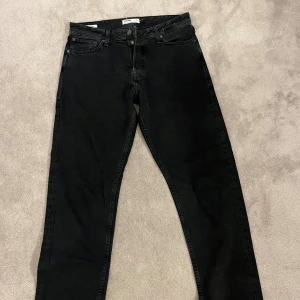 Svarta jeans från Jack & Jones - Säljer ett par svarta jeans från Jack & Jones i klassisk femficksmodell. Jeansen har rak passform, normal midja och är tillverkade i slitstarkt bomullsmaterial. Snygga detaljer med svarta nitar och logopatch baktill i midjan.