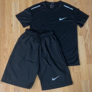 Svarta träningsshorts från Nike - Svarta träningsshorts från Nike med klassisk vit swoosh-logga på benet. Shortsen har elastisk midja med snörning för skön passform och är tillverkade i lätt polyester som andas. Perfekta för gymmet eller sport, loose fit och stilren design.