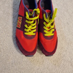 Rosa sneakers från Helly Hansen - Säljer ett par snygga sneakers från Helly Hansen i rosa och mörklila med limegula snören och HH-logga på sidan. Skorna har en grovmönstrad sula för extra grepp, rund tå och detaljer i mocka och syntet. Perfekt för dig som gillar färgstarka skor med cool design.