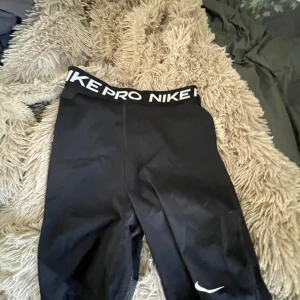 Nike Pro svarta träningstights-shorts - Svarta Nike Pro shorts med vit logga på benet och bred resår i midjan med Nike Pro-tryck. Tight passform och stretchigt material som passar perfekt till träning eller sport. Klassisk och sportig look, midwaist modell. XS storlek använd 2 gånger max