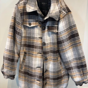 Rutig overshirt från Name It - Riktigt snygg rutig overshirt från Name It i beige, brunt och vitt. Jackan har klassisk krage, knäppning med knappar framtill och två bröstfickor med lock. Perfekt för lager-på-lager och chill stil.