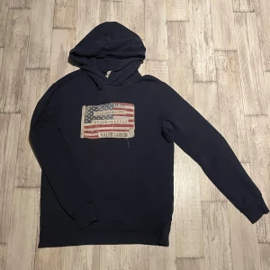 Mörkblå hoodie från Ralph Lauren - Väldigt eftertraktad hoodie från Ralph Lauren Denim & Supply med amerikansk flagga tryckt på bröstet. Tröjan har huva och är tillverkad i 100% bomull. Perfekt för en avslappnad stil. !(Storlek S men sitter som M)!