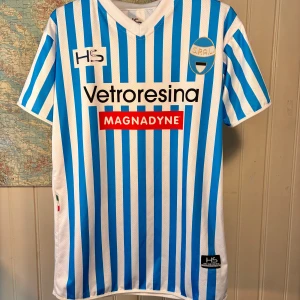 S.P.A.L 2016/17 HS hemmatröja, storlek L - Säljer en officiell SPAL fotbollströja från HS i storlek L. Tröjan är vit med blå vertikala ränder, har klubbmärke på bröstet och flera sponsorer tryckta fram och bak. Tillverkad i lätt och ventilerande polyester, perfekt för match eller träning.